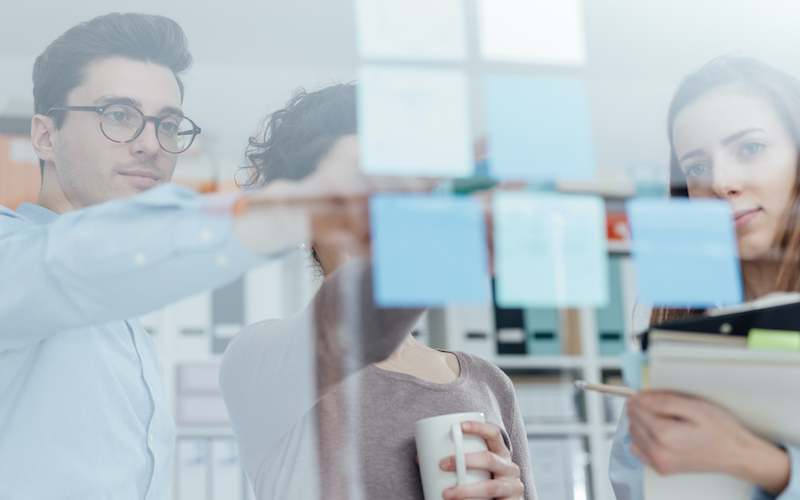 Junges Team trifft sich im Büro Junge Geschäftsleute team Sitzung im Büro und arbeiten zusammen, sie besprechen Ideen auf klebrigen Anmerkungen und finden neue kreative Lösungen, Start und Unternehmergeistkonzept